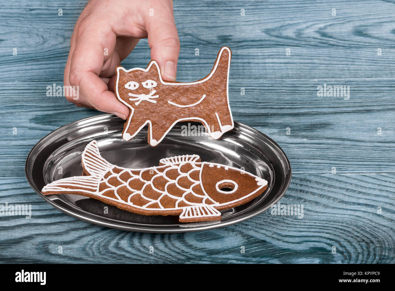 Gatto e pesce. Carino gingerbreads natale su un vassoio d'argento Mano umana tenendo il dolce kitty al di sopra della piastra lucida blu su uno sfondo di legno. Foto Stock