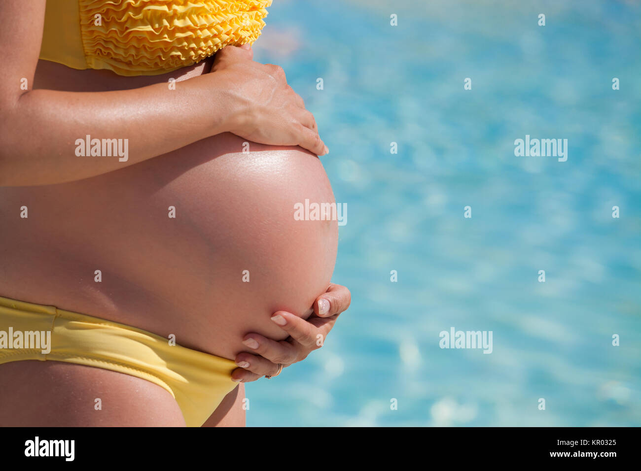 Donna incinta con le mani sulla pancia di fronte a un pool Foto Stock