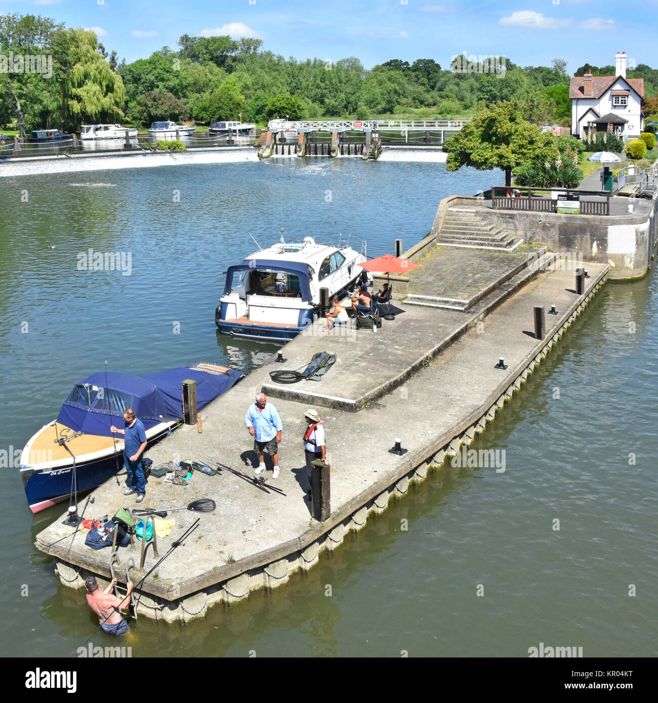 Guardando verso il basso a partire da sopra a approccio al Goring Lock sul Fiume Tamigi in Oxfordshire con pescatori e del motore di lancio passeggeri bloccare i detentori cottage oltre Foto Stock