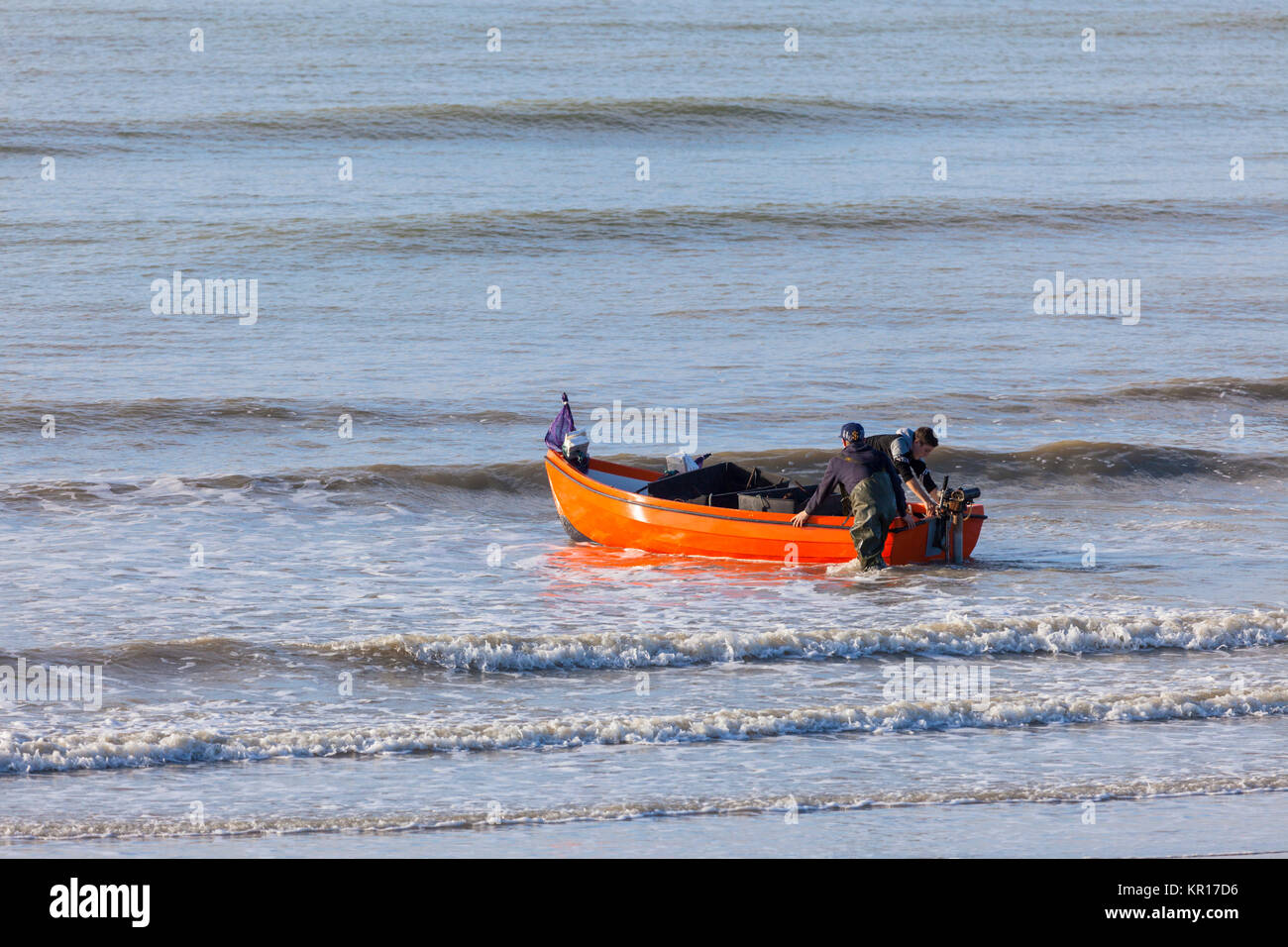 Due giovani uomini lanciando una piccola barca in mare in Hastings Foto Stock