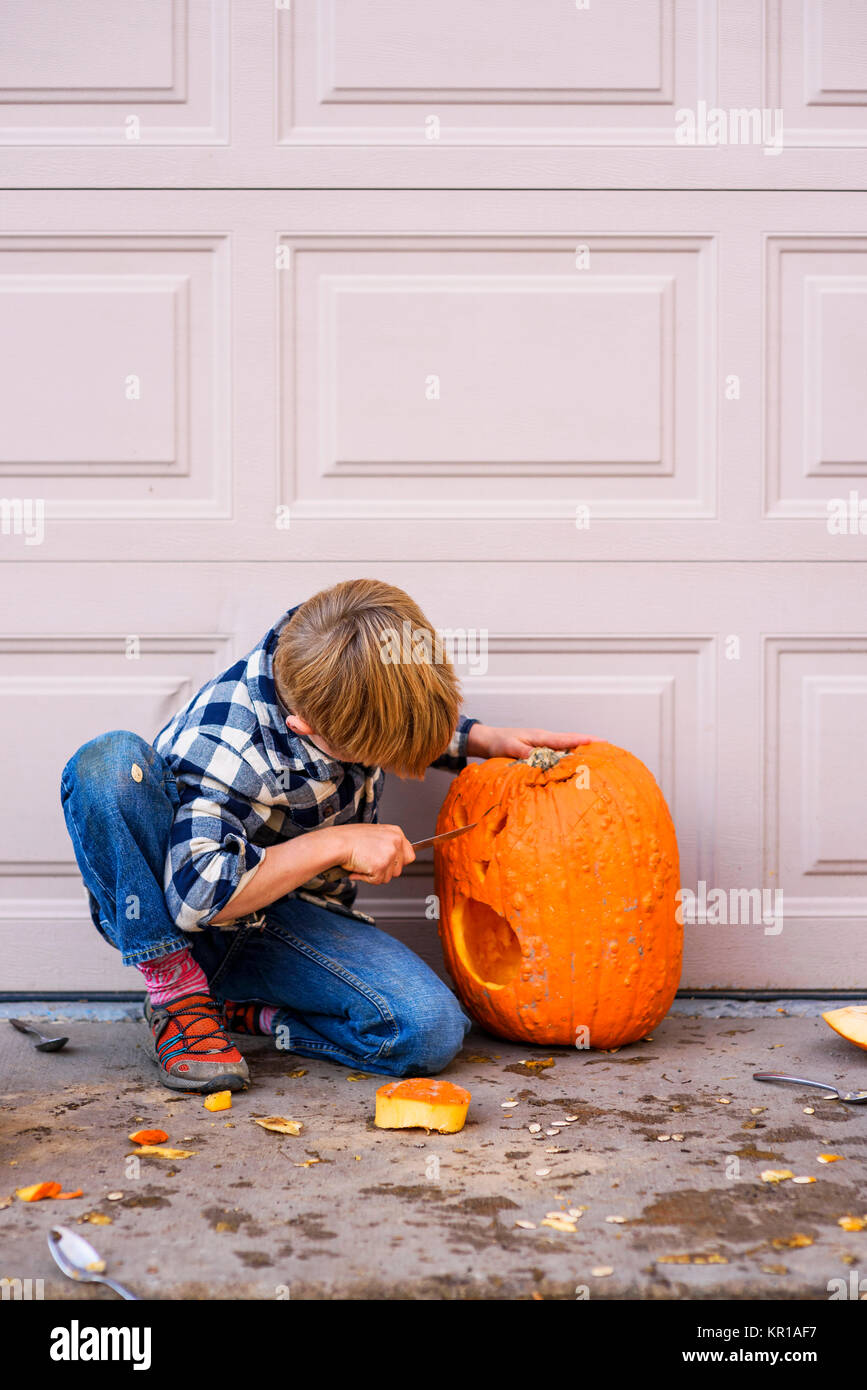 Ragazzo inginocchiato all'aperto intagliare una zucca di Halloween Foto Stock