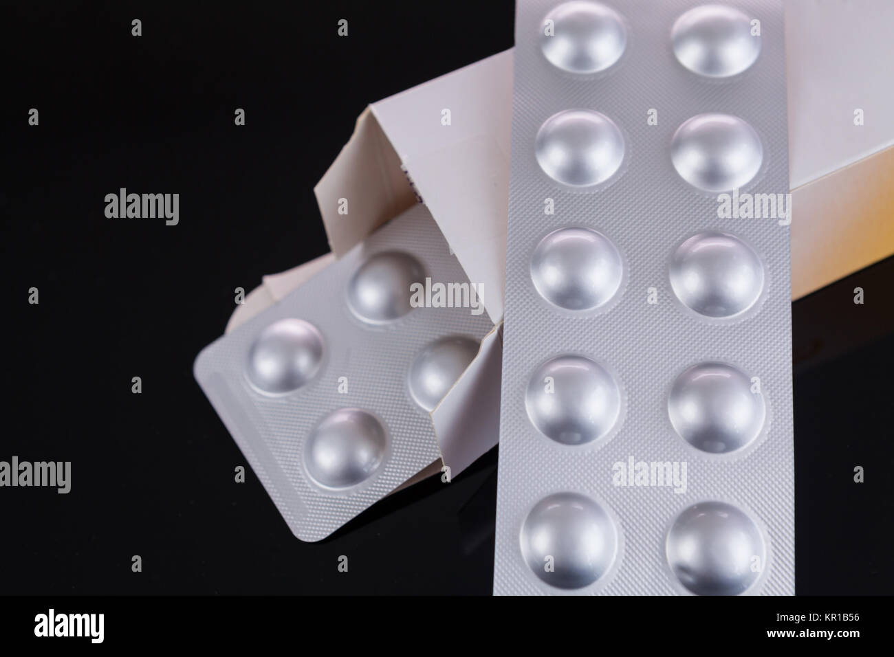 Silberne Blisterpackung von kleinen Pillen zusammen mit Schachtel mit zusätzlichen Packungen durch den offenen Deckel über einem schwarzen Hintergrund in einem Gesundheits-Konzept Foto Stock