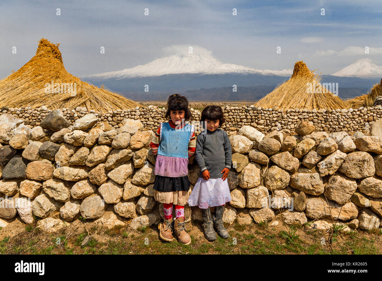 Due ragazze locali con le due cime del Monte Ararat e pile di canne sullo sfondo ad Agri, Turchia. Foto Stock