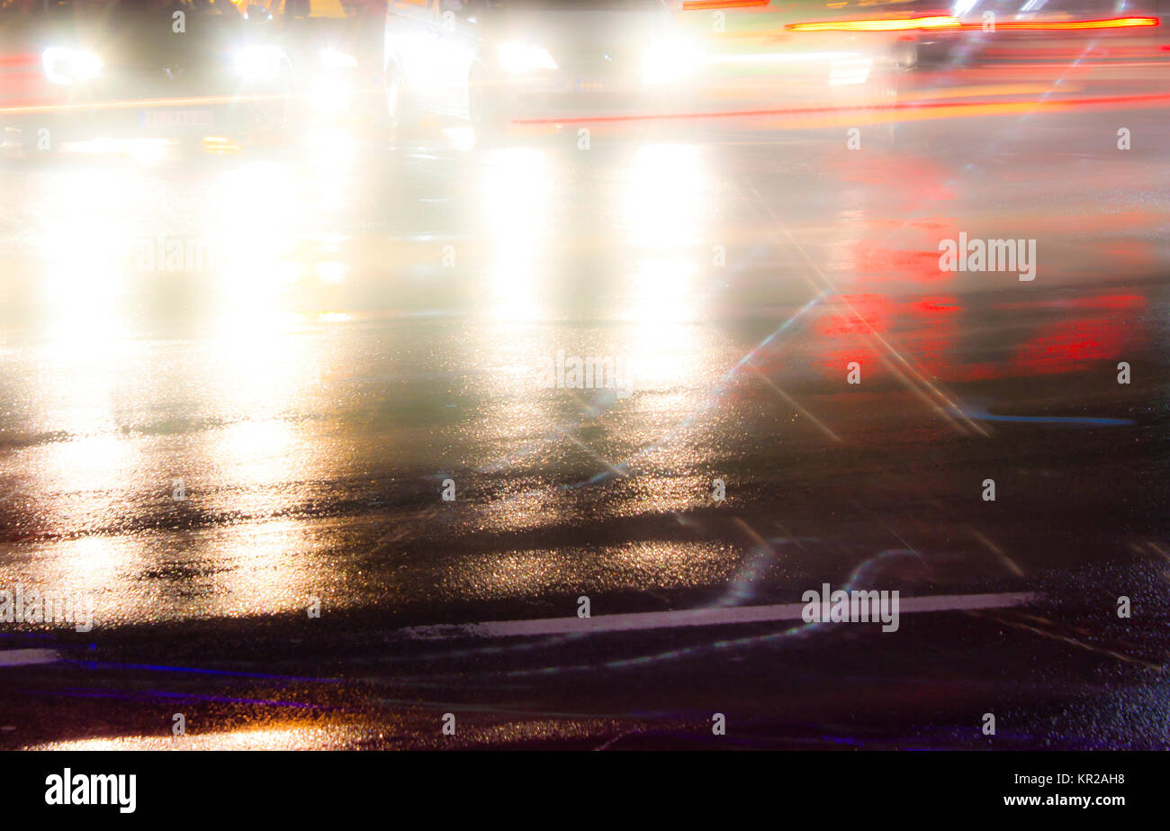 Sfocato il traffico notturno di pioggia per le strade delle città intersezione con sentieri di luce e di riflessi su asfalto umido. Foto Stock