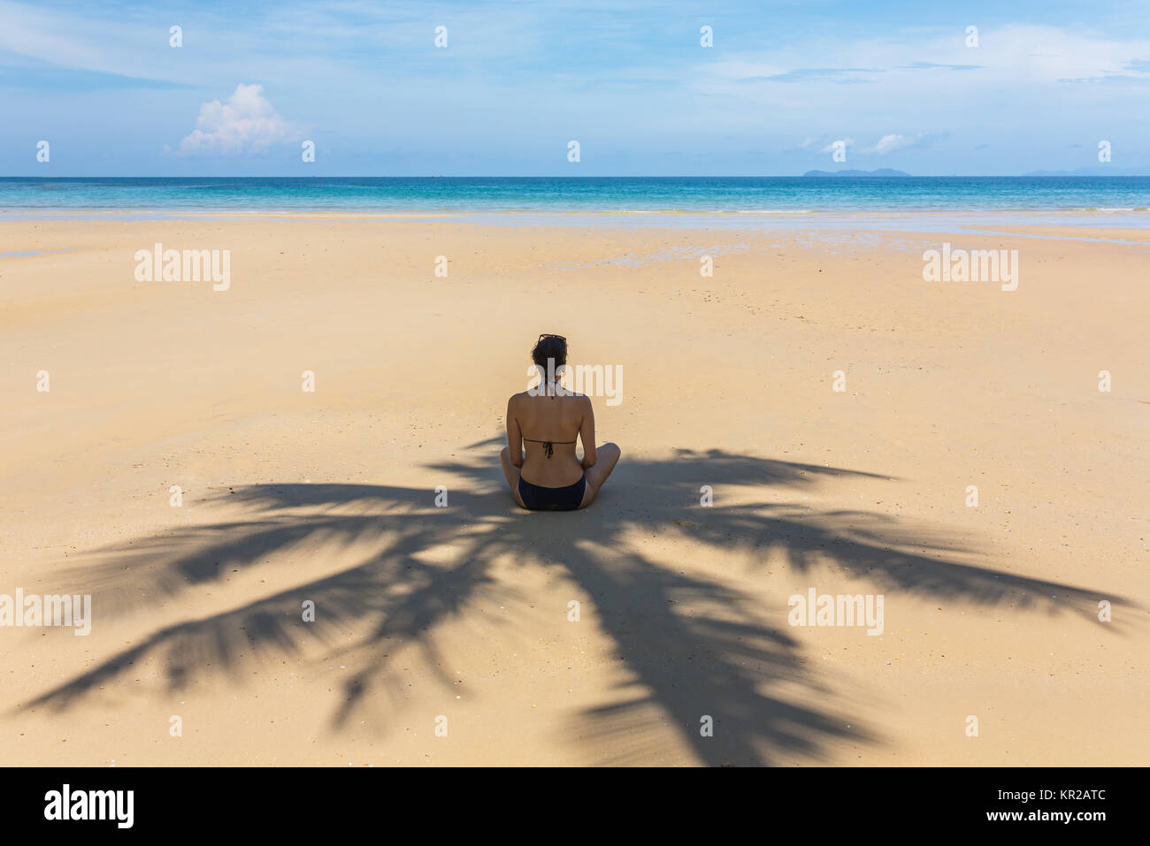 Giovane donna seduta all'ombra di palme sulla spiaggia tropicale di Koh Kood island, Thailandia Foto Stock