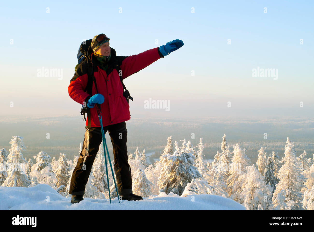 Alpinista con uno zaino e bastoni per il trekking a piedi mostra una mano alla distanza, in piedi in cima alla montagna in inverno gelido scenario Foto Stock