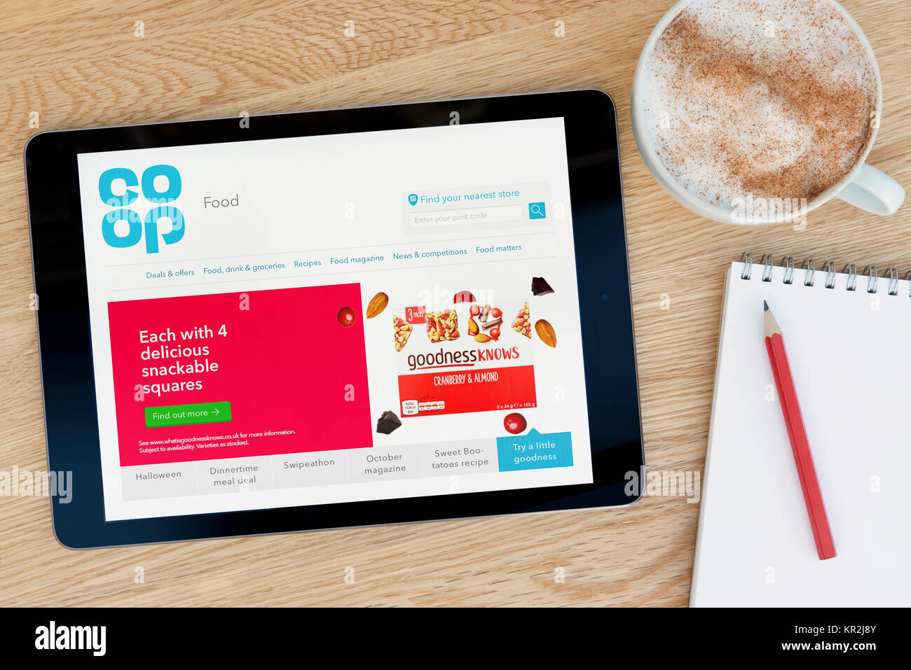 La Coop cibo sito su un iPad dispositivo tablet pc che si appoggia su una tavola di legno accanto a un blocco note e matita e una tazza di caffè (editoriale solo) Foto Stock