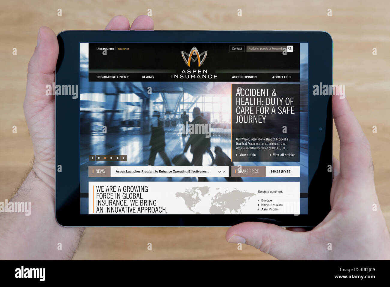 Un uomo guarda all'Aspen sito di assicurazione sul suo iPad dispositivo tablet, sparato contro un tavolo di legno top sfondo (solo uso editoriale) Foto Stock