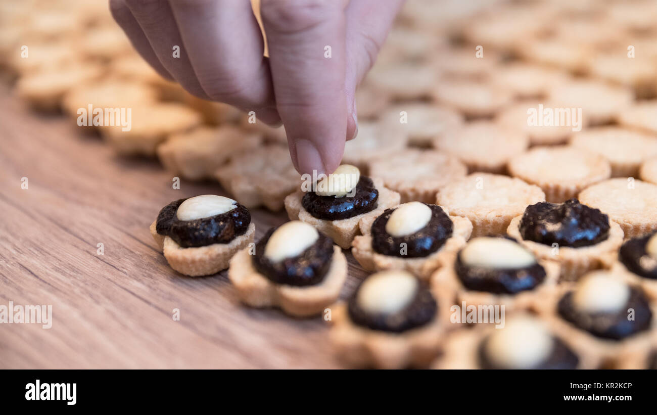 Realizzazione di dolci tortini di cioccolato con ripieno di mandorle e. Dettaglio della mano femminile mentre la decorazione della noce di cocco pasticceria natale su fondo in legno. Foto Stock