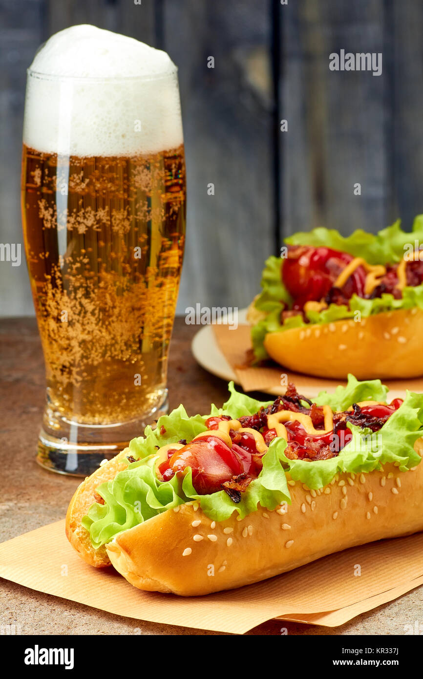 Due hot dogs con condimenti e bicchiere di birra Foto Stock