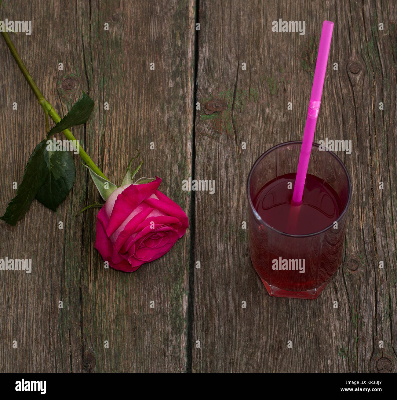 Una rosa rossa e un bicchiere di succo di frutta, su un vecchio tavolo Foto Stock