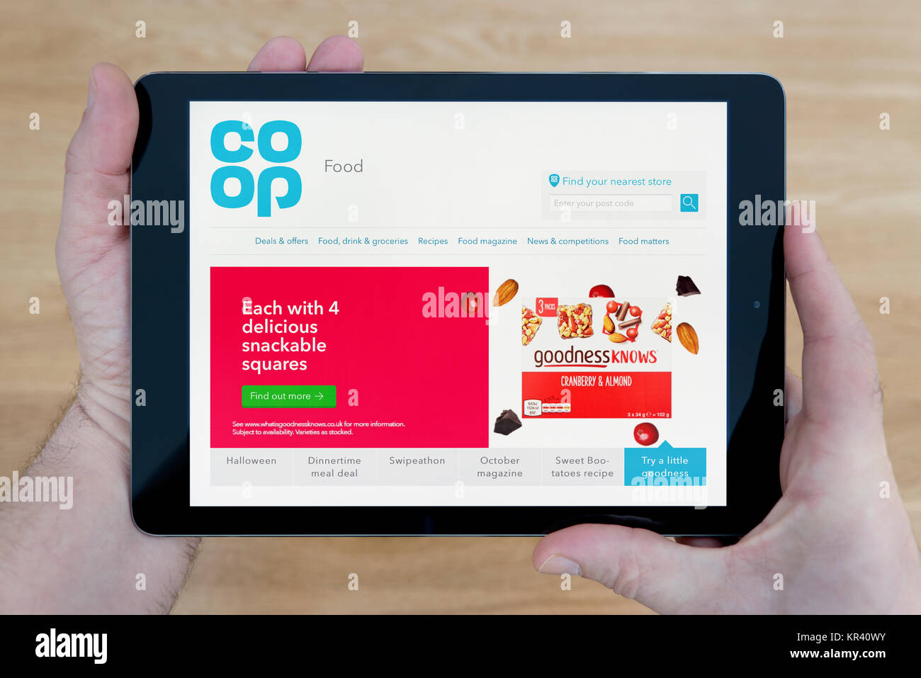 Un uomo guarda la Coop cibo sito sul suo iPad dispositivo tablet, sparato contro un tavolo di legno top sfondo (solo uso editoriale) Foto Stock