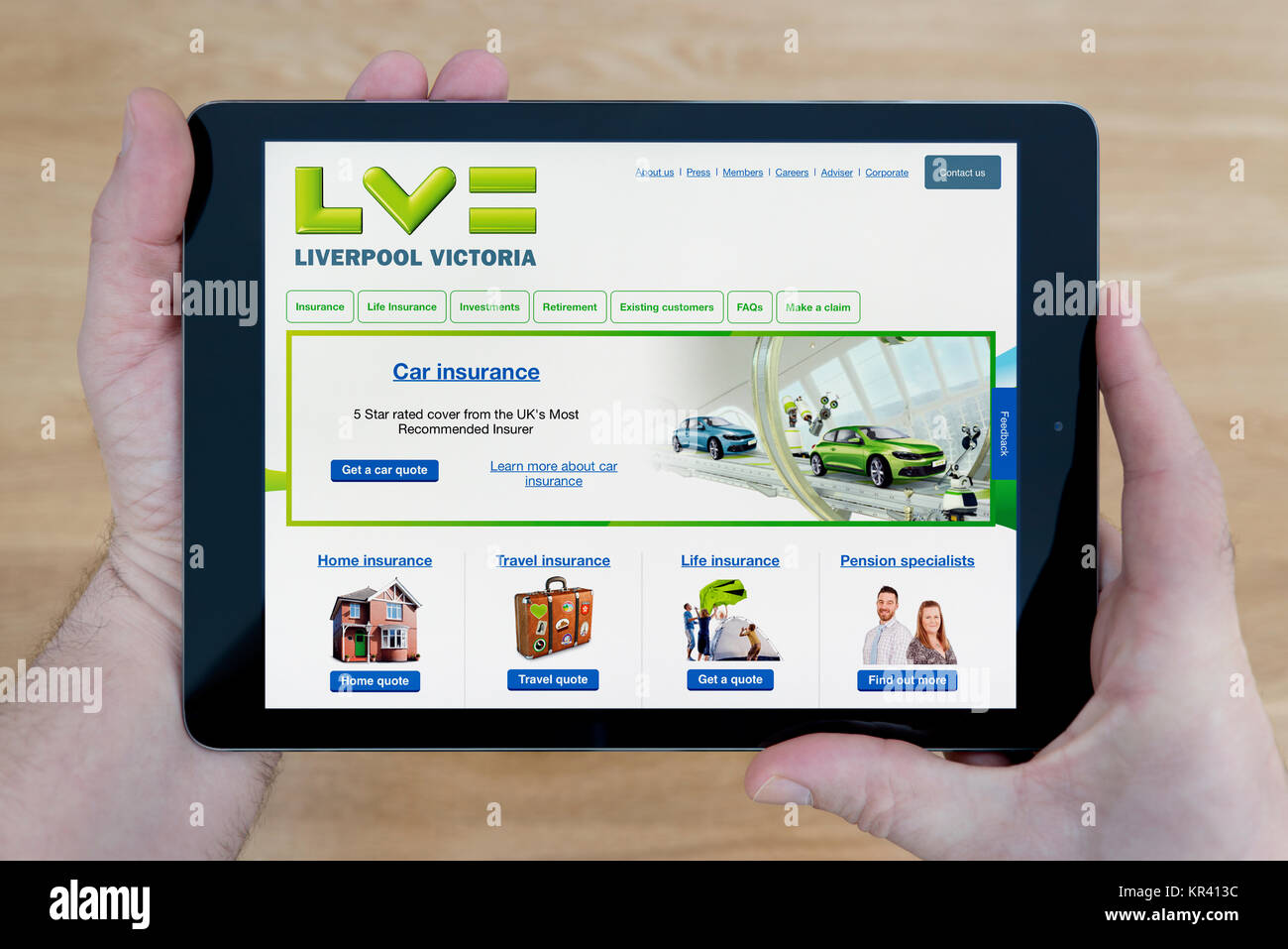 Un uomo guarda il Liverpool Victoria sito sul suo iPad dispositivo tablet, sparato contro un tavolo di legno top sfondo (solo uso editoriale) Foto Stock