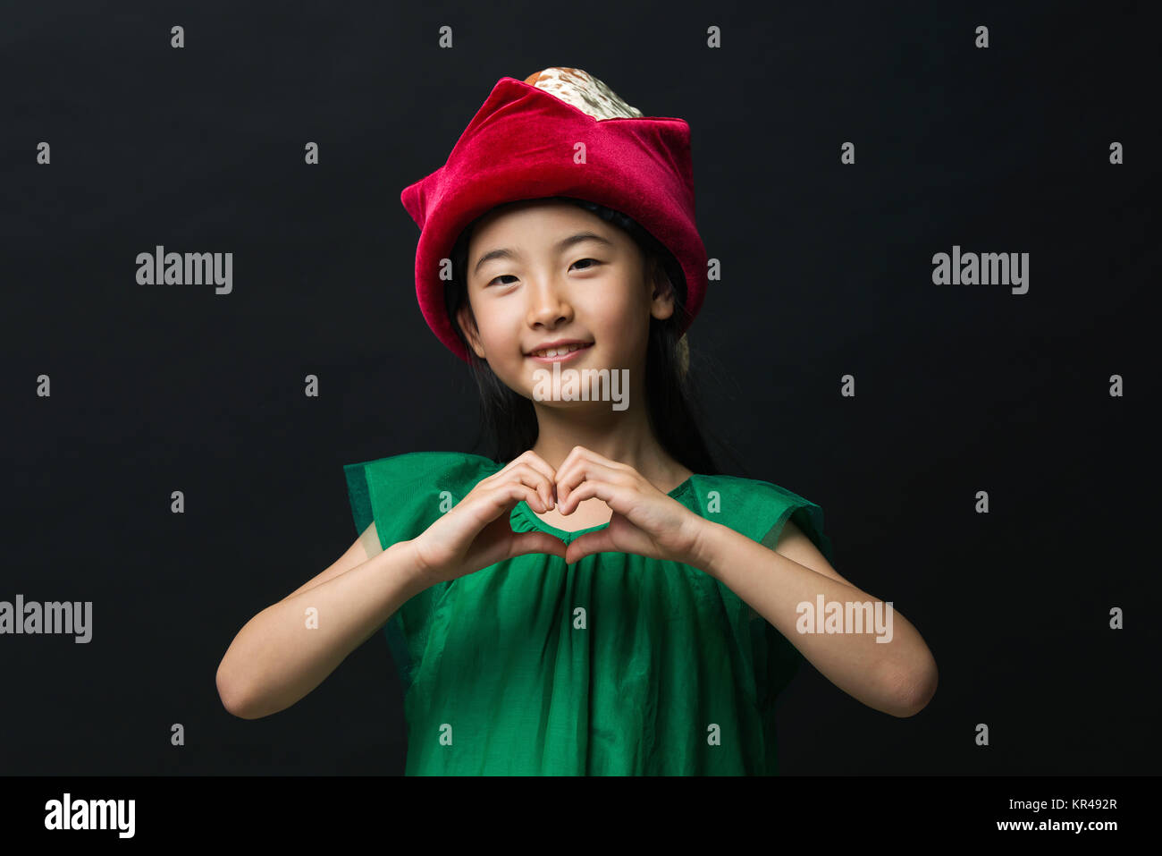 Carino ragazza asiatica vestita in fairy hat e fatti a mano cuore, vestito di verde su sfondo nero. Foto Stock