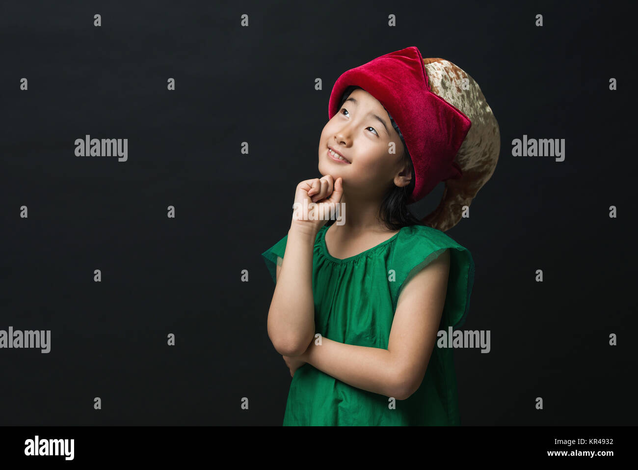 Carino ragazza asiatica vestito con un abito verde con una fata hat su uno sfondo nero, con un'idea di pensare. Foto Stock