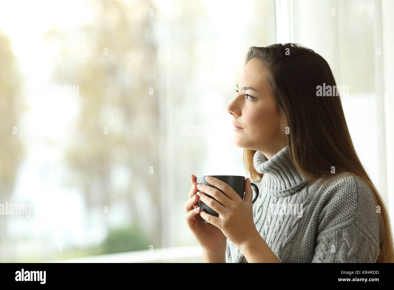 Vista laterale verticale di un pensieroso grave donna di guardare attraverso una finestra a casa in un giorno triste Foto Stock