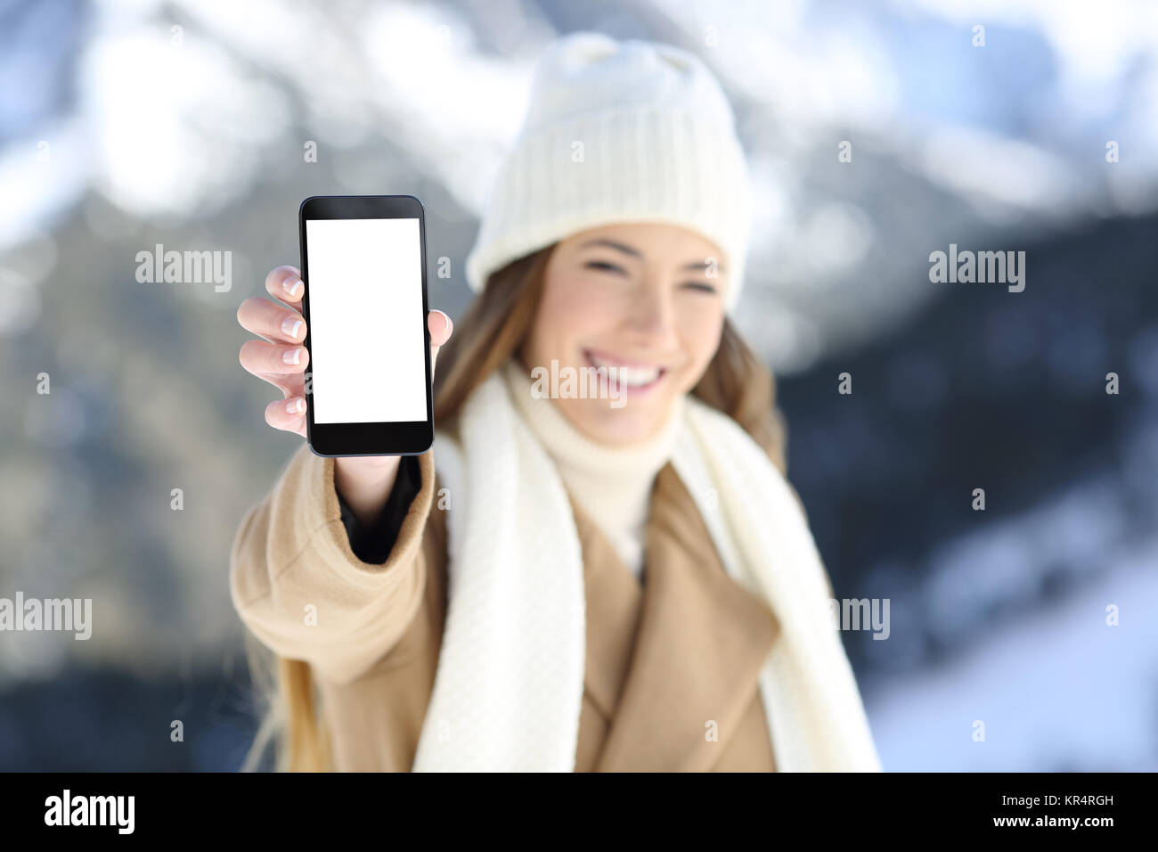 Vista Fronf ritratto di una donna che mostra a mano un telefono intelligente schermo vuoto in vacanze invernali in una montagna innevata Foto Stock