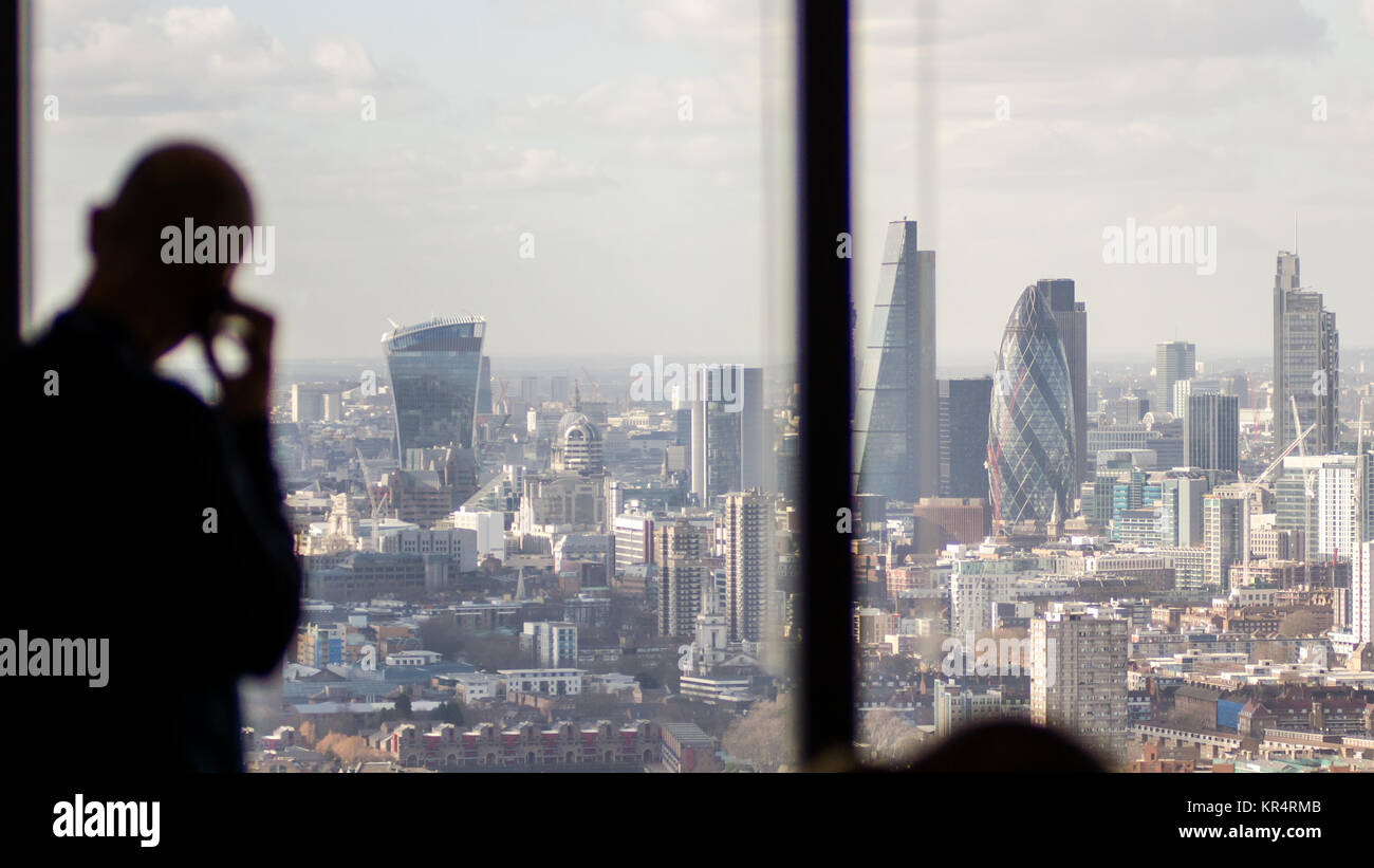 London, England, Regno Unito - 27 Febbraio 2015: un uomo di affari di effettuare una chiamata su un telefono cellulare si stagliano nella finestra di un ufficio Docklands grattacielo, Foto Stock