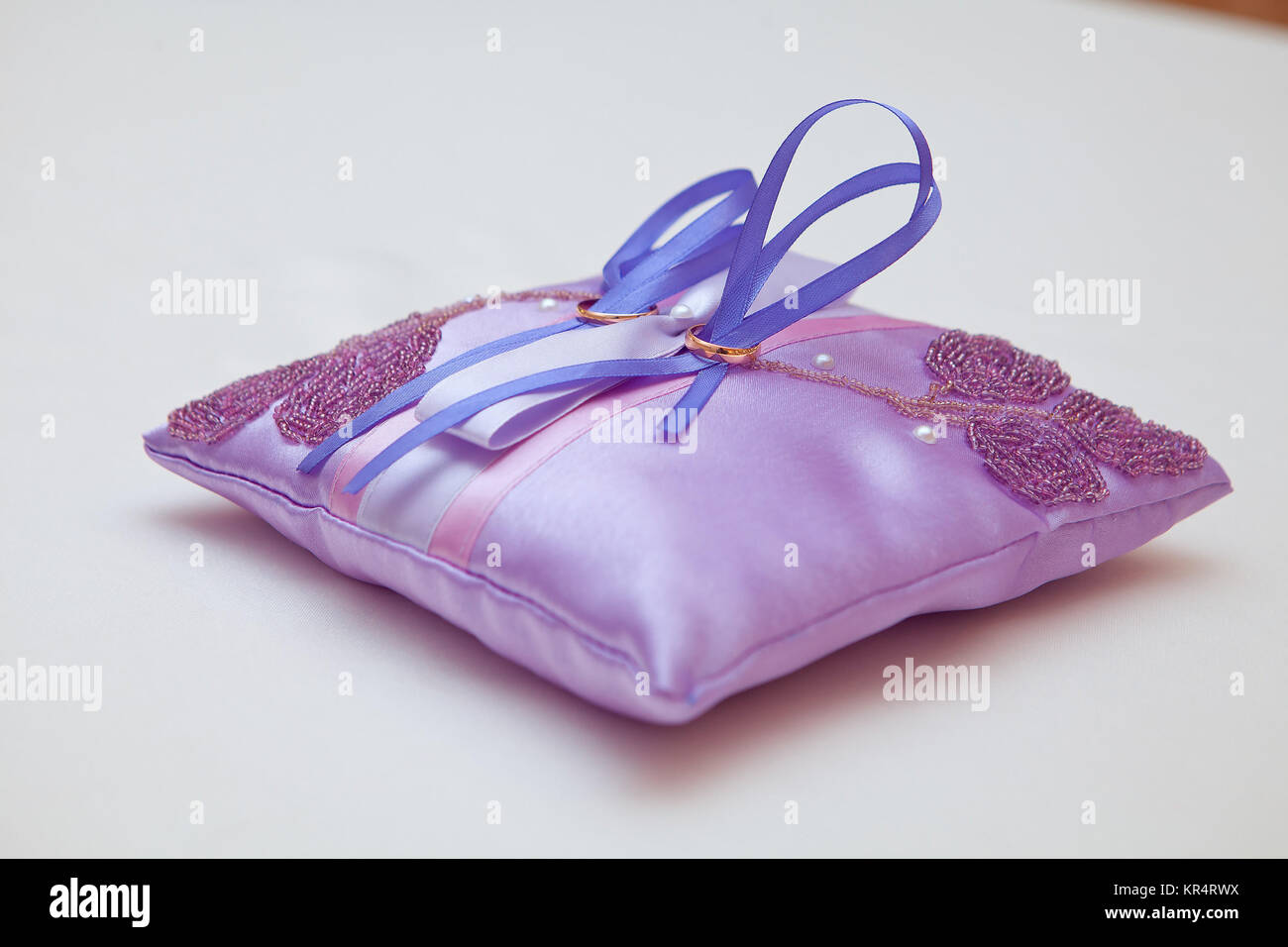 Oro anelli di nozze su un cuscino bianco in attesa di scambio. Gli anelli legati con il cuscino da utilizzando il nastro bianco su uno sfondo bianco. Foto Stock