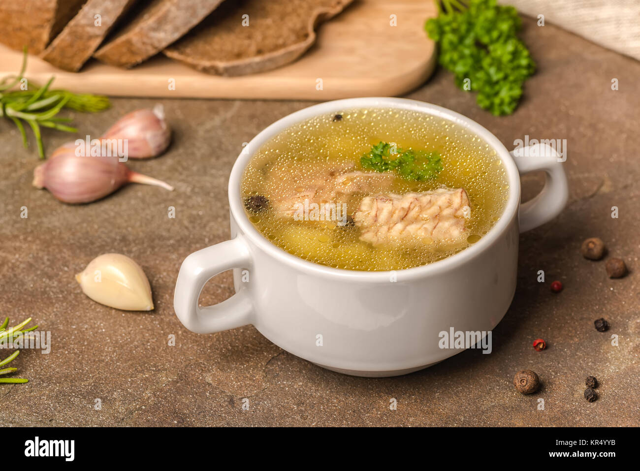 Trasparente fresca zuppa di pesce con lo storione, patate in piastra bianca, decorato di aglio, foglie di prezzemolo e tagliate il pane di segale, mangiare sano Foto Stock