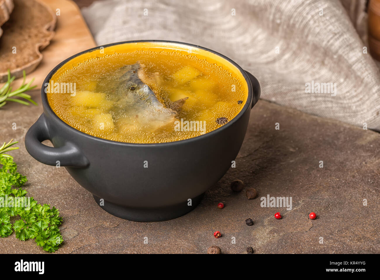 Trasparente la zuppa di pesce con lo storione, patate in piastra nera, decorato di aglio, prezzemolo in foglie, il cucchiaio di legno e tagliate il pane di segale, spazio di copia Foto Stock