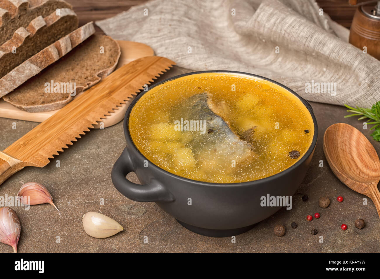 Trasparente la zuppa di pesce con lo storione, patate in piastra nera, decorato l'aglio, il cucchiaio di legno e tagliate il pane di segale, mangiare sano Foto Stock