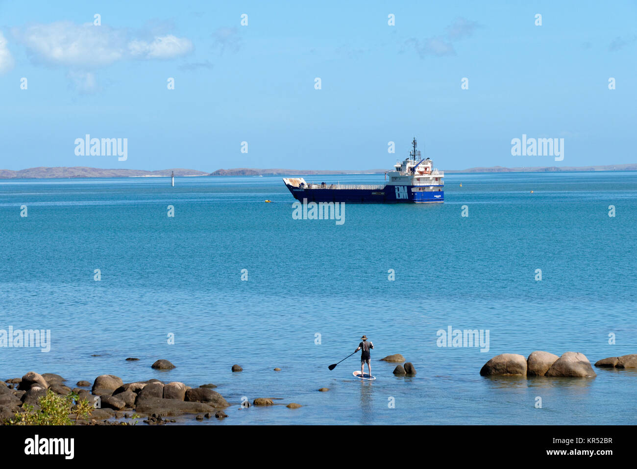 Uomo in piedi sulla scheda di racchetta con la barca in distanza, Dampier, Pilbara, Australia occidentale Foto Stock