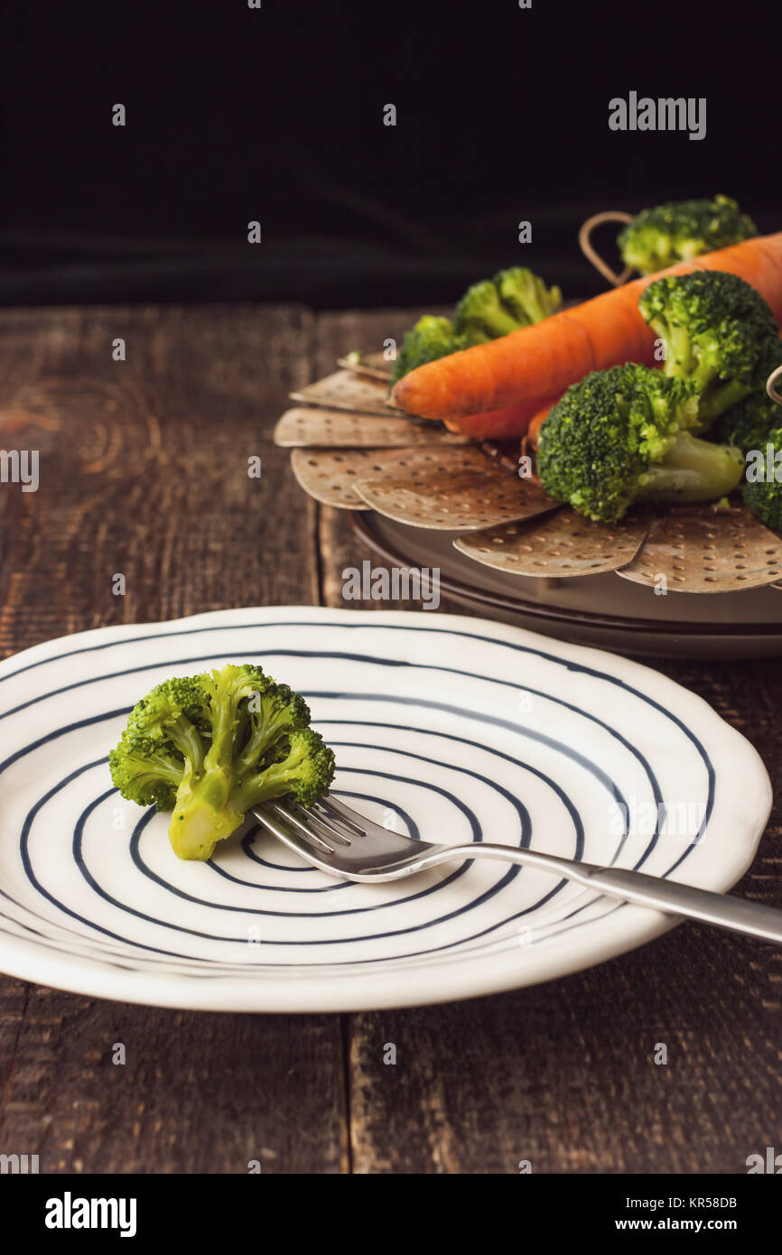 Broccoli cotti al vapore su una forcella sulla piastra di ceramica in verticale Foto Stock