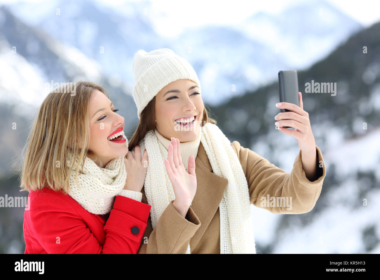 Due turisti felici avente una chiamata video con uno smart phone in vacanze invernali in una montagna innevata Foto Stock