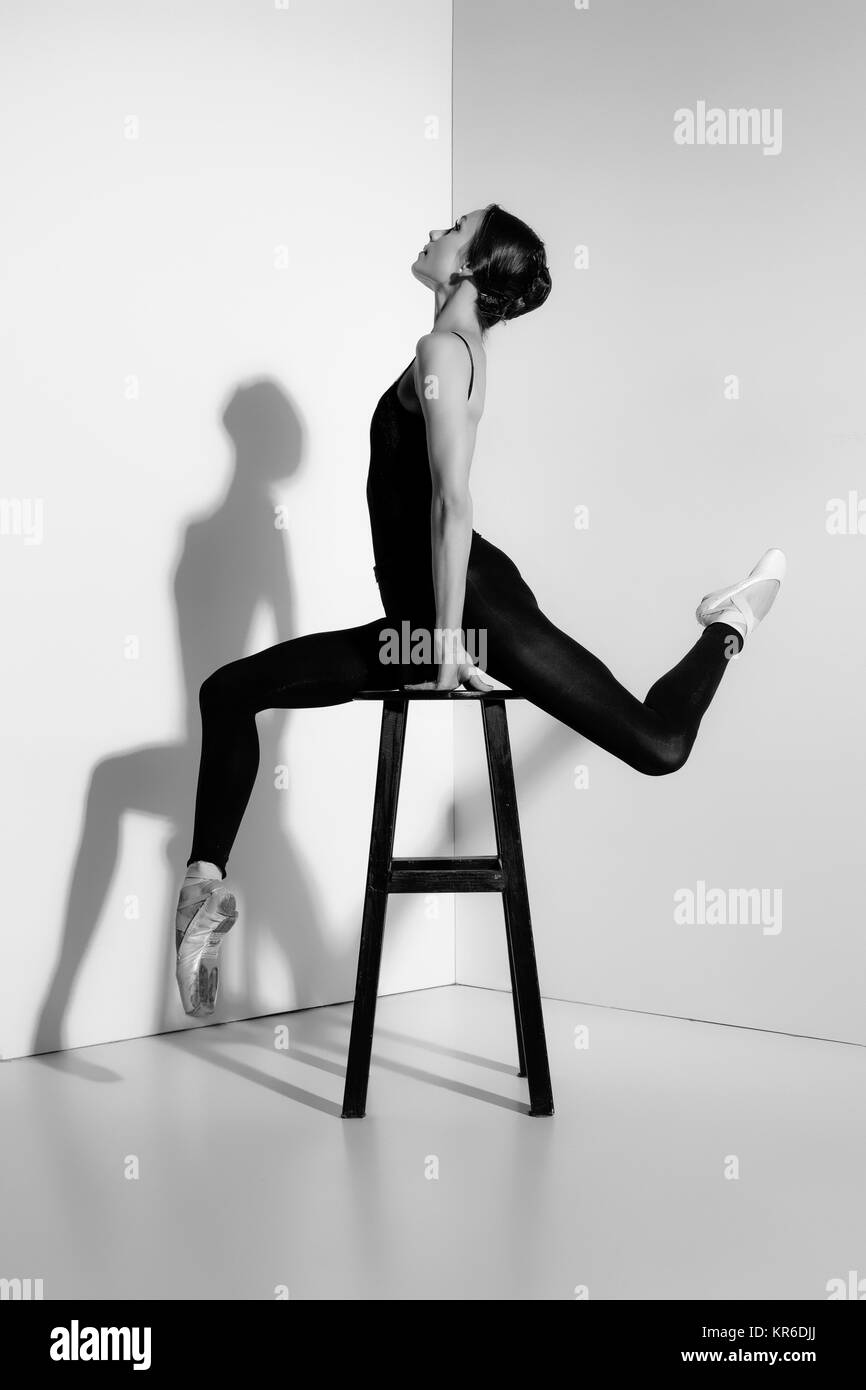 Ballerina in abito nero in posa su una sedia in legno, di sfondo per studio. Foto Stock