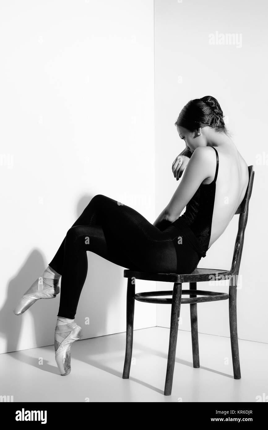 Ballerina in abito nero in posa su una sedia in legno, di sfondo per studio. Foto Stock