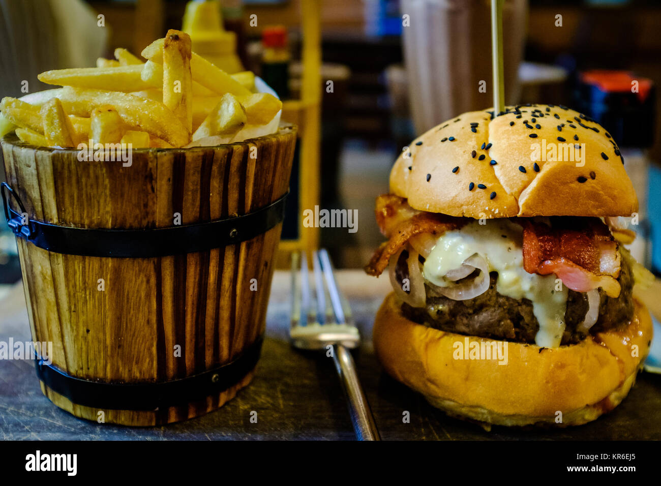 Gustano un delizioso hamburger con cipolle, bacon, formaggio blu e succosa carne di Bangkok. Sideorder: una benna di patatine fritte Foto Stock