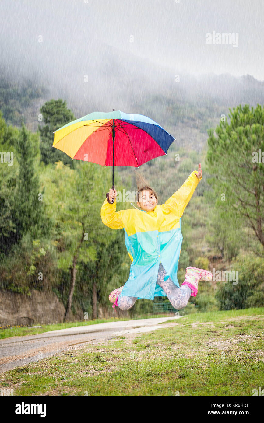 Bambina con ombrello coloratissimo,impermeabile e stivali impermeabili  giocare sotto la pioggia Foto stock - Alamy