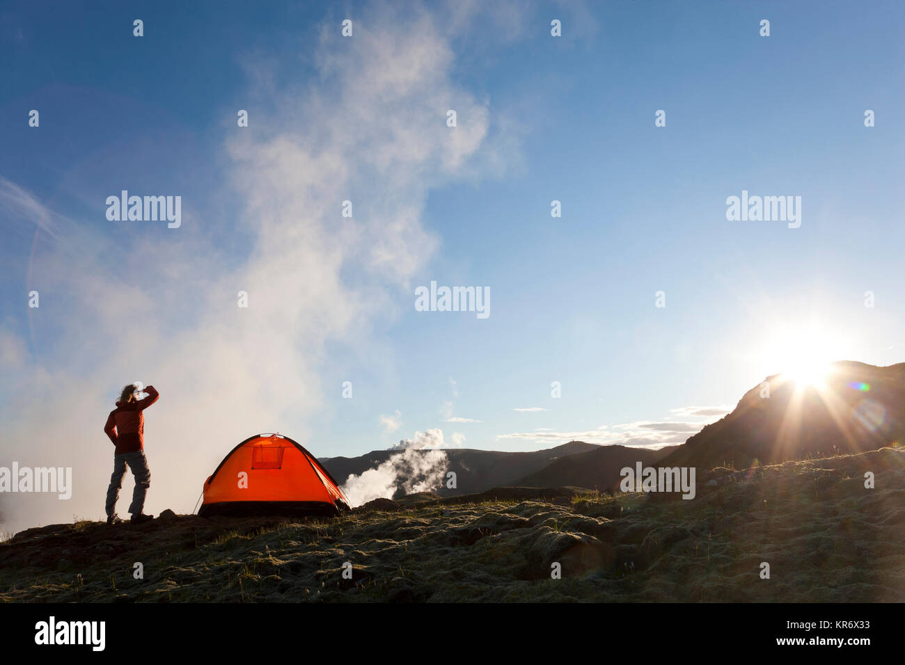 Donna in piedi in montagna, accanto a una tenda, sunrise. Foto Stock