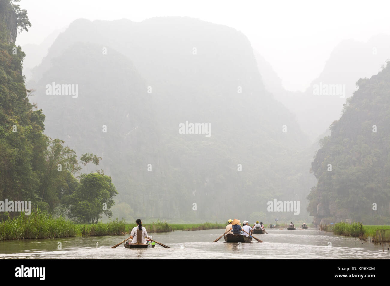 Gruppi di persone in imbarcazioni a remi sulle rive di un fiume e le montagne sullo sfondo. Foto Stock