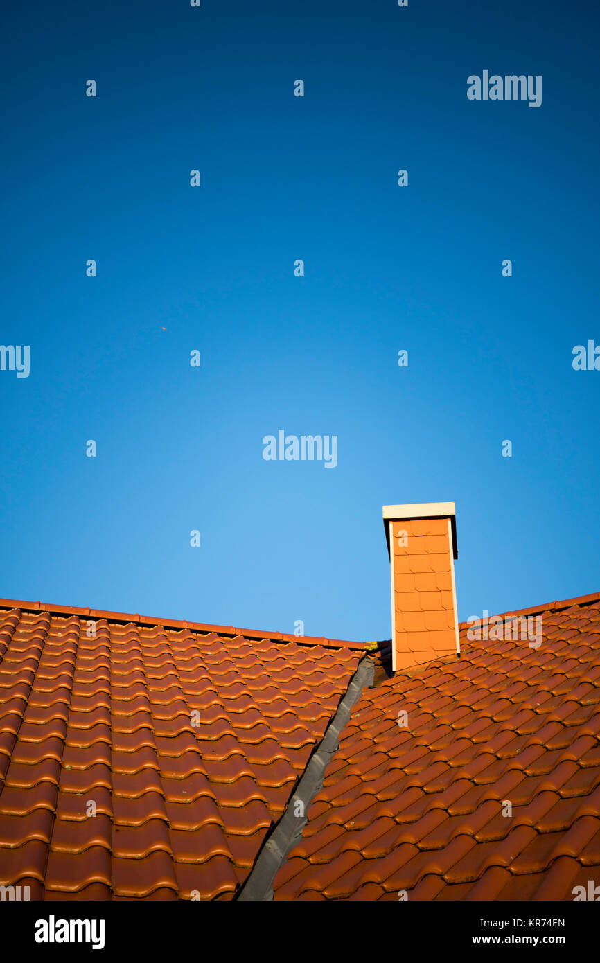 Il tetto rosso con mattonelle di terracotta e il camino di fronte blu cielo senza nuvole Foto Stock