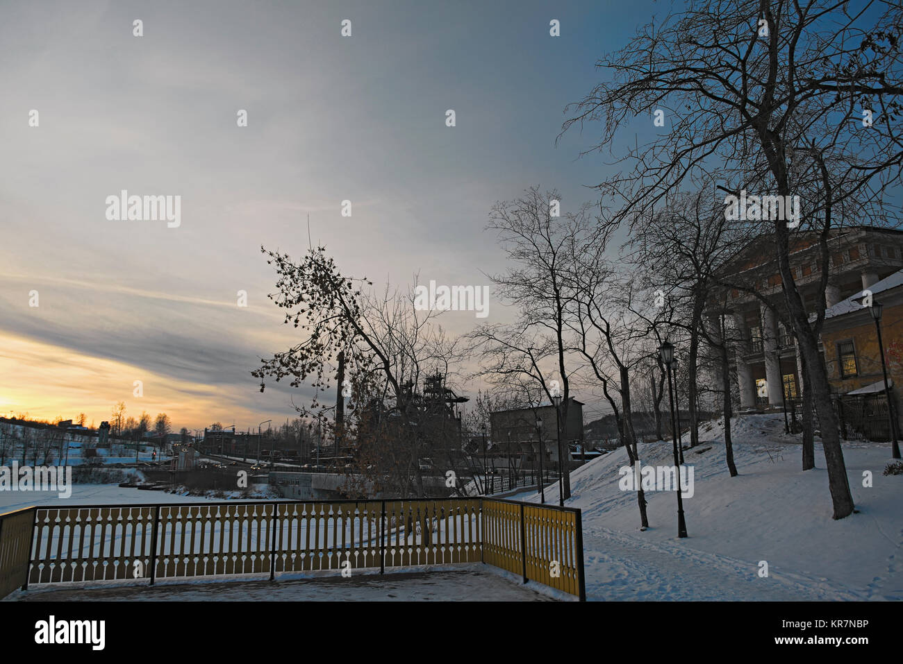 Paesaggio invernale con campo nevoso, alberi sfrondato e lago ghiacciato nel parco della città. Foto Stock