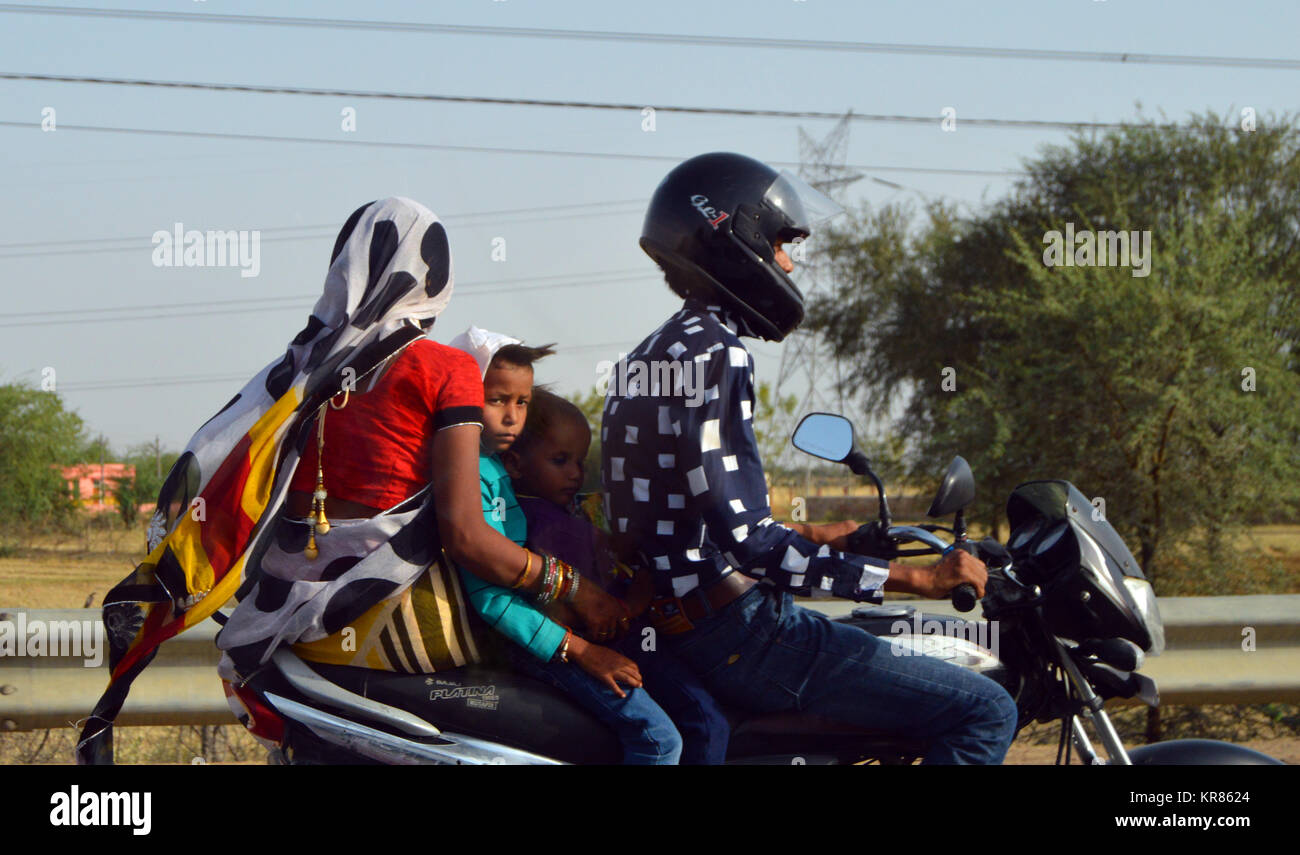 Famiglia su moto con solo il conducente indossa un casco su strada di Agra, India. Ragazzo che guarda alla telecamera. Foto Stock