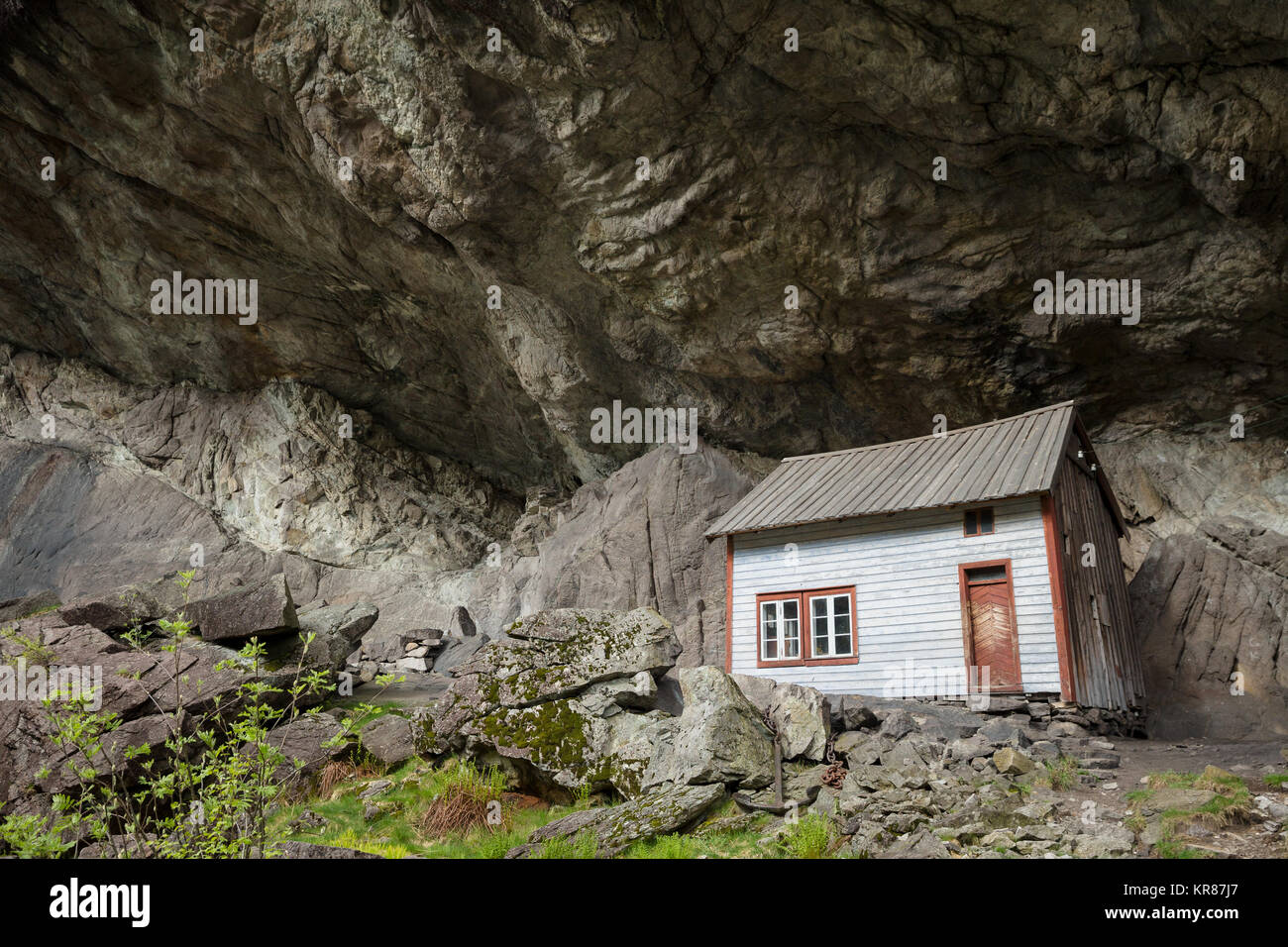 Abbandonato vecchie case in legno risalente all'ottocento sostare sotto un enorme roccia a strapiombo chiamato Helleren formando un tetto naturale - Jossingfjord, Norvegia Foto Stock