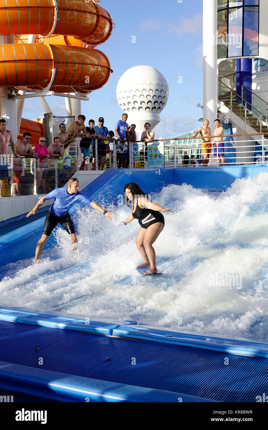 Un operatore aiuta a un passeggero di crociera imparare a navigare sulla nave di Flowrider. Foto Stock