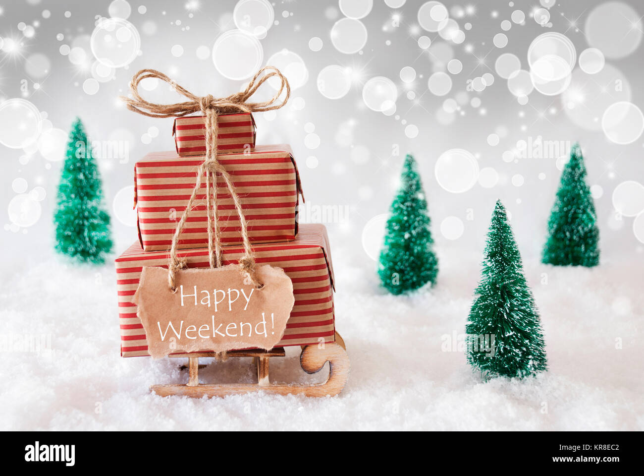 Una slitta o slitta con i regali di Natale o presenta. Scenario innevato con neve e alberi. Spumante bianco con sfondo bokeh effetto. Etichetta con testo in inglese Happy Weekend Foto Stock