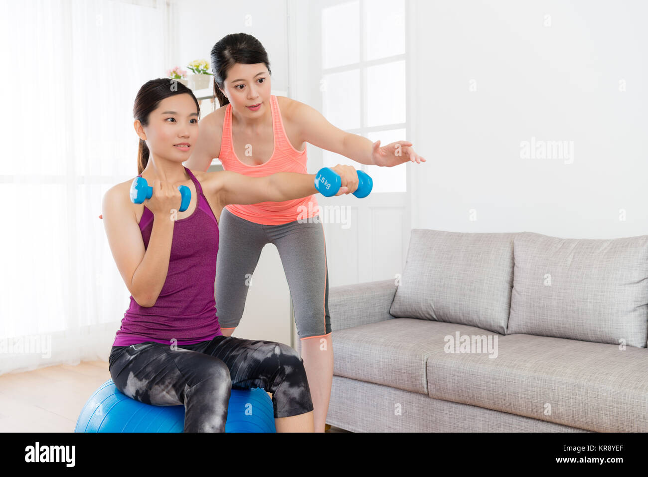Attraente bellezza studentessa seduti sulla sfera di yoga e tenendo il manubrio rendendo il pugilato gesto corpo di allenamento con la sua casa fitness teacher. Foto Stock