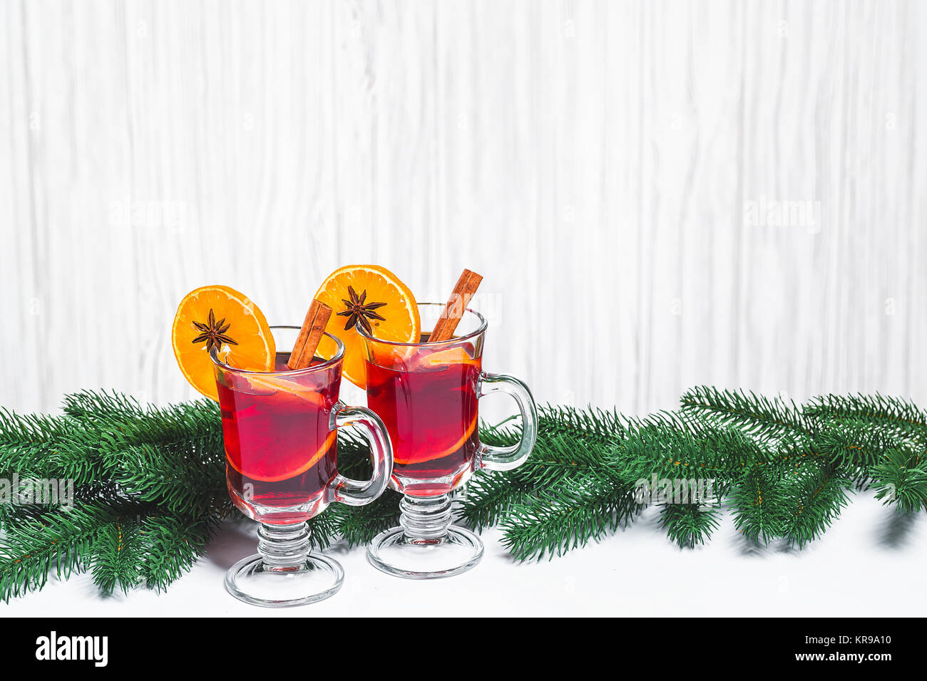 Natale di vetro rosso vino mulled sul tavolo con bastoncini di cannella, rami di albero di Natale in bianco sullo sfondo di legno. Spazio libero Foto Stock