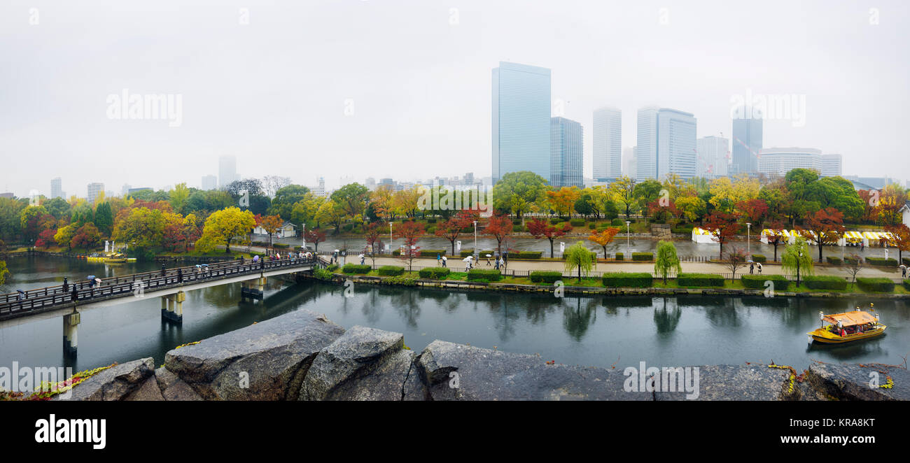 Il parco del Castello di Osaka canal con battelli turistici e ponte Gokurakubashi panoramica autunno brumoso paesaggio urbano con Chuo-ku financial district torre alta Foto Stock