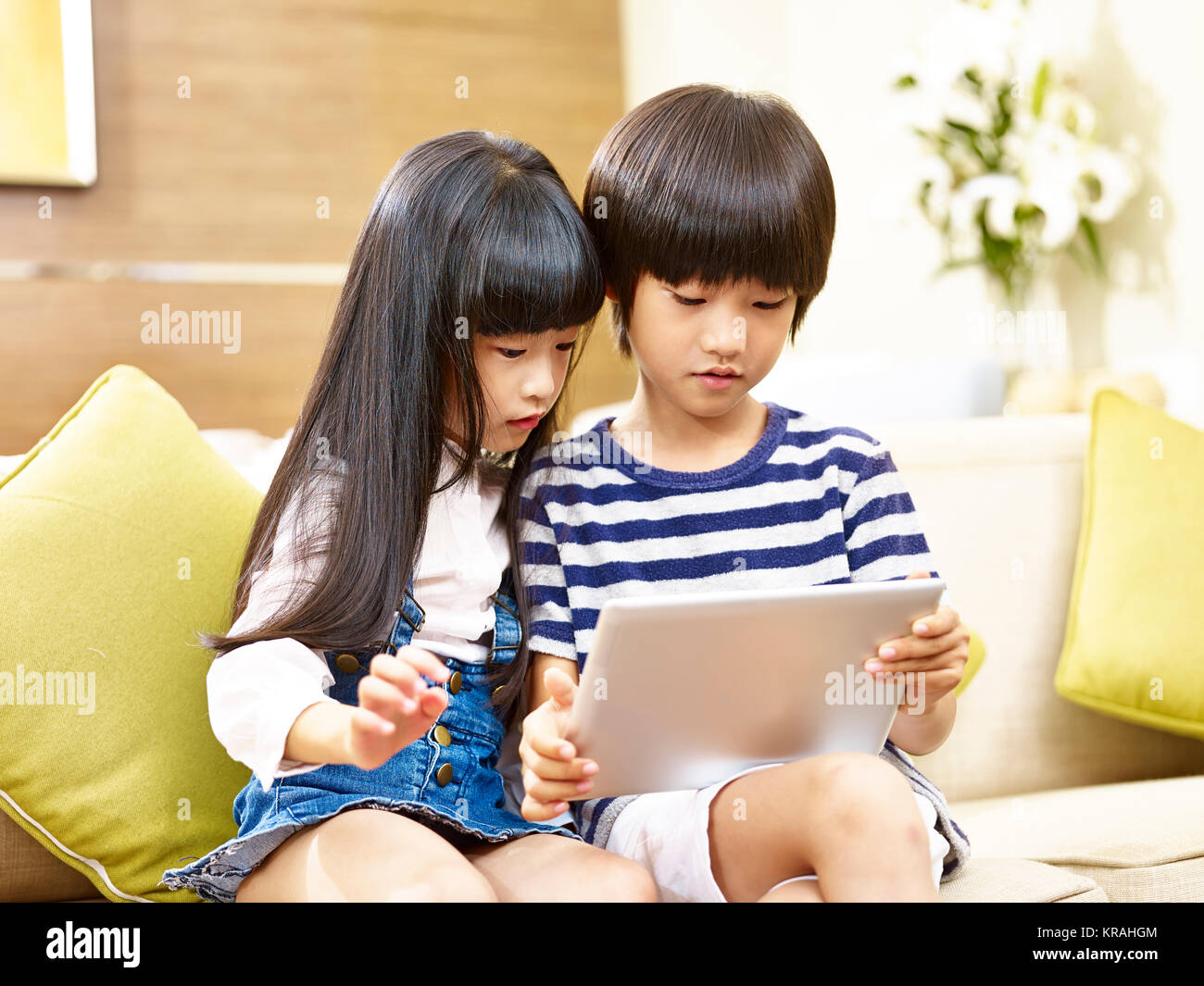 Asian fratello e sorella seduti sul divano guardando a tavoletta digitale insieme. Foto Stock