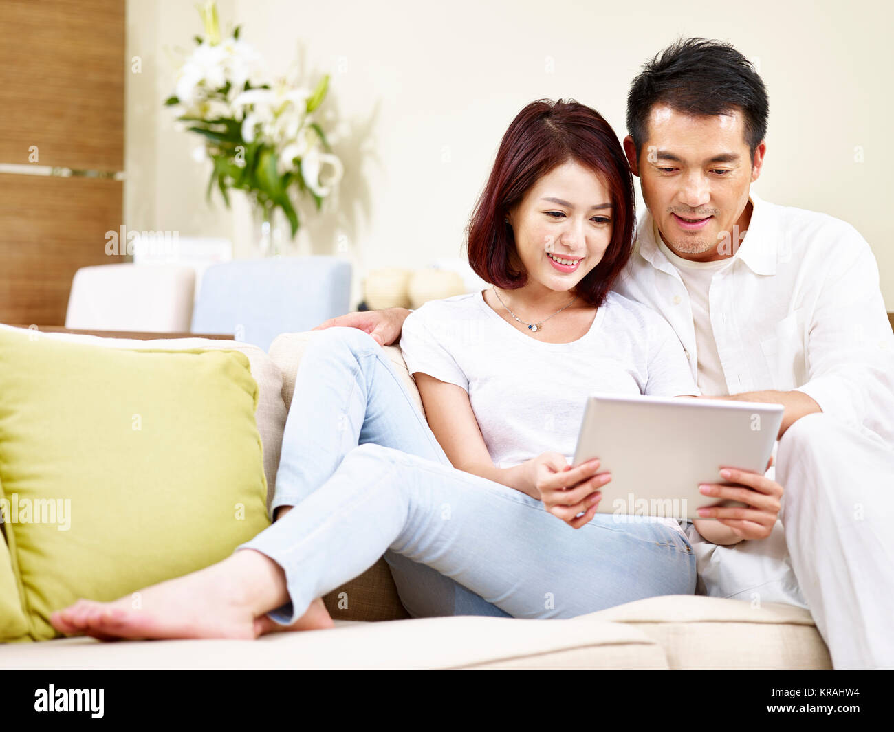 Asian giovane seduto sul divano di famiglia in soggiorno con tavoletta digitale insieme. Foto Stock