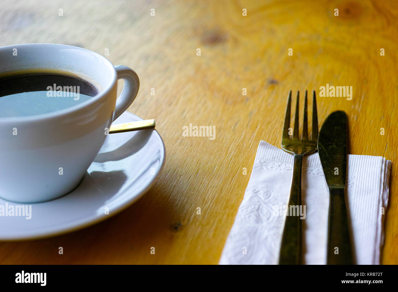 Il cafe ristorante tavolo in legno con tazza di caffè, ottone posate e tovagliolo bianco. Moderna caffetteria tabella con oro colorered forcella, un cucchiaio e un coltello e sal Foto Stock