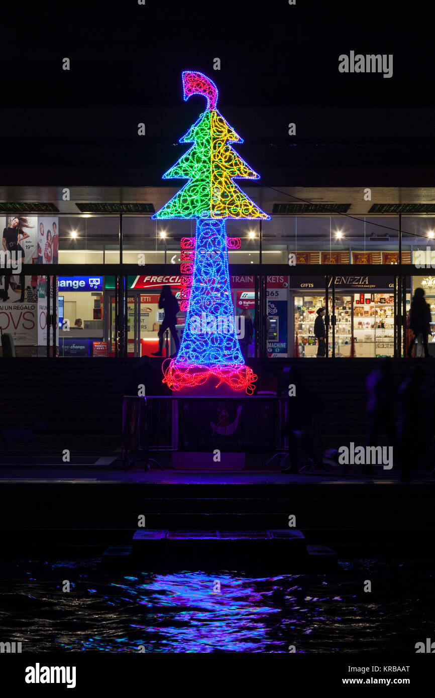 Le luci di Natale al di fuori la stazione Santa Lucia di Venezia sotto forma di un albero di Natale con gondola ferro si riflettono sul Canal Grande di notte Foto Stock