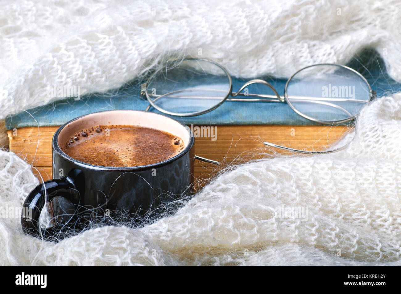 Una tazza di caffè avvolto in una sciarpa, maglione o caldi plaid, con un libro e occhiali. In autunno o inverno, fine settimana, vacanza o di mattina di buon concetto. Clos Foto Stock