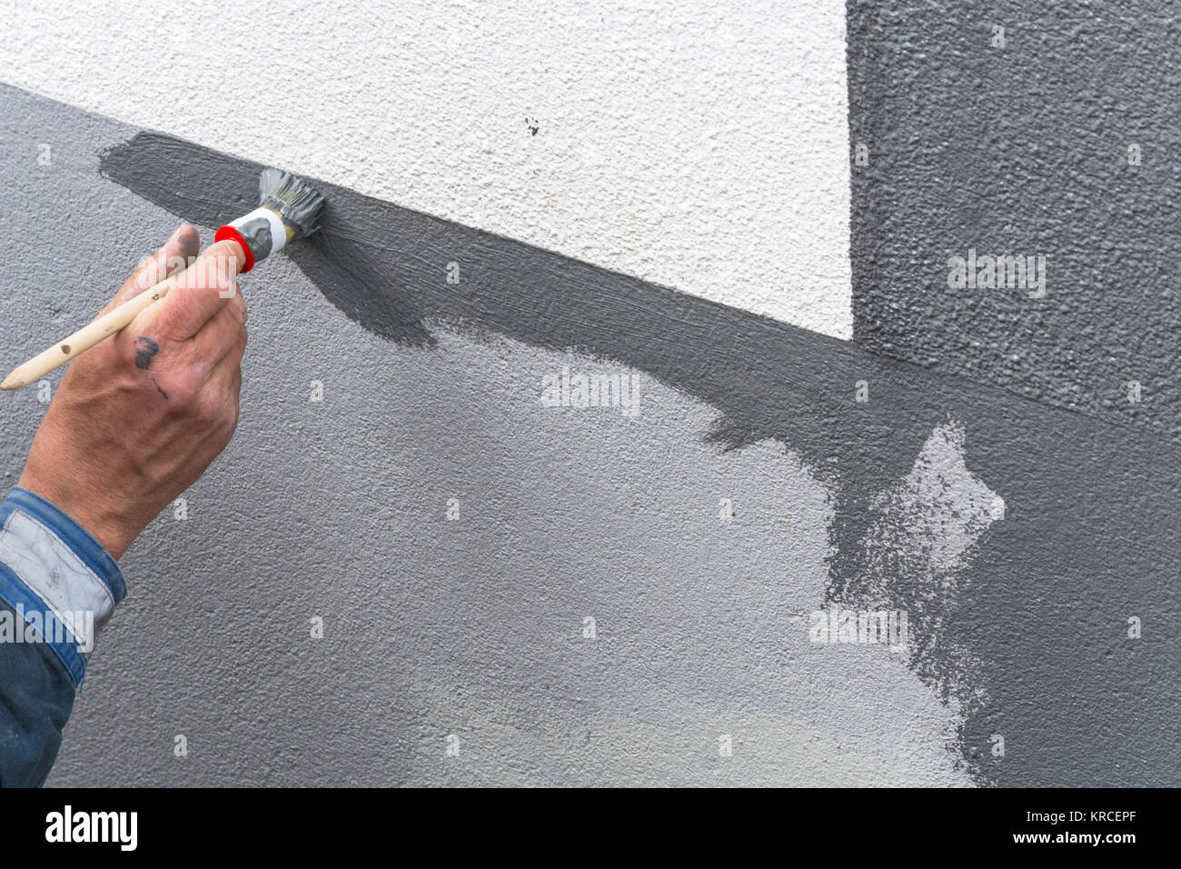 Braccio Nahaufnahme eines Anstreicher mit Farbrolle in der mano streicht eine Hauswand mit grauer Farbe. Foto Stock